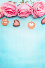 Pink roses with heart chocolate and romantic love message on blue background, top view. Valentine's Day or Birthday greeting card