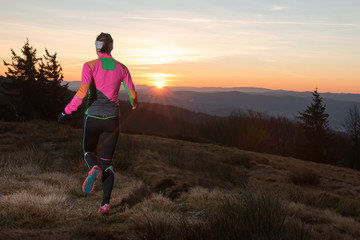 young woman running in the mountains to the sun in the cold spring morning 