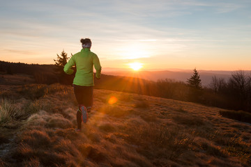 woman from back running on the trail in the mountains with first ray of light in the morning