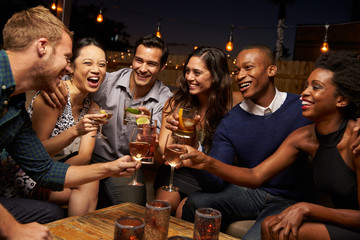 Group Of Friends Enjoying Night Out At Rooftop Bar - obrazy, fototapety, plakaty