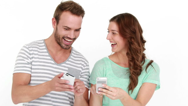 Smiling couple texting and standing back to back
