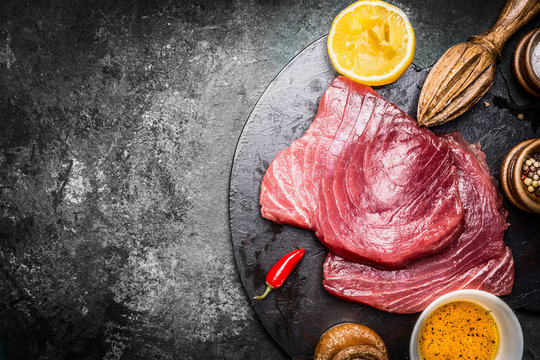 Raw Tuna fish steaks with ingredients for grill or cooking on dark vintage background, top view, place for text