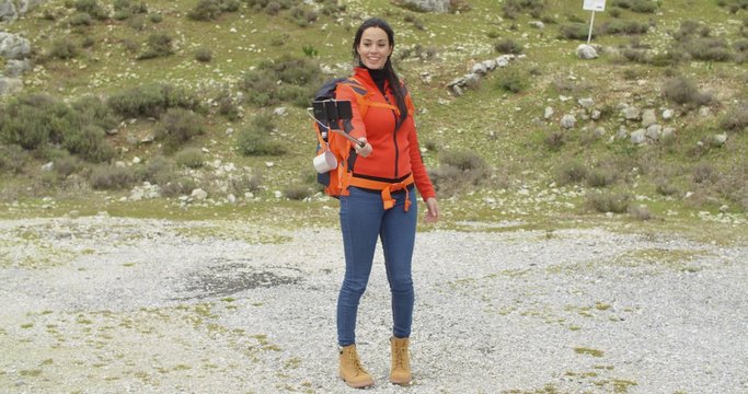 Smiling young backpacker using a selfie stick to take her photograph on a smart phone as a memento of her hike in the mountains