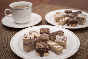 Different types of cookies on the white plate and coffee in the white cup. Ambient restaurant light. Selective focus.