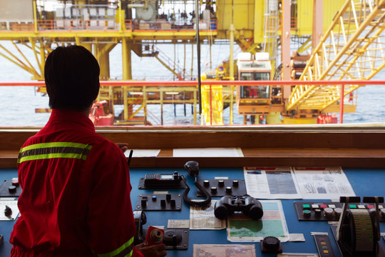A helmsman on the bridge of a supply vessel nearby an offshore oil-rig