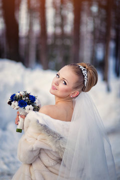 bride posing in the winter forest in a fur coat. Wedding photo