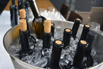 Mehrere teilweise geöffnete Weinflaschen in einem Metallkübel, der mit Eiswürfeln gefüllt ist.