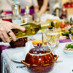 Human hand pours a white wine to wineglass