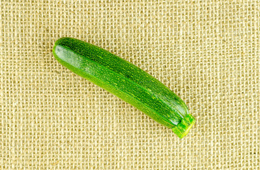 Single baby zucchini against burlap