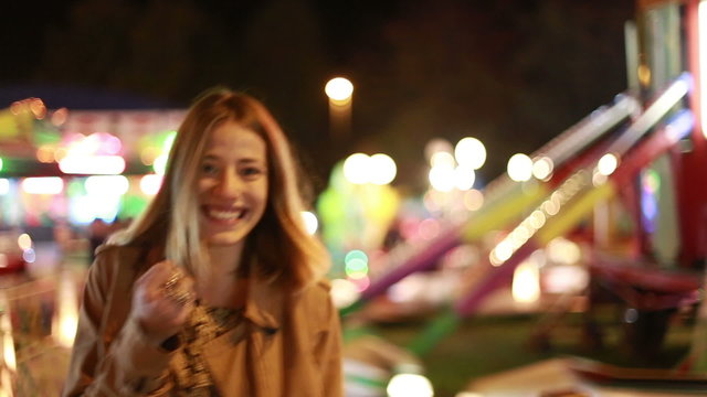 Young woman laughing and waving at camera in amusement park