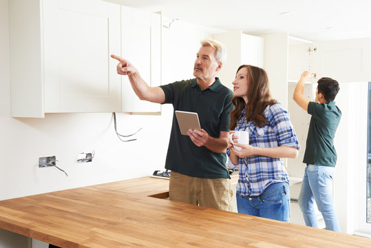 Woman With Carpenter Looking At Plans For Kitchen On Digital Tab
