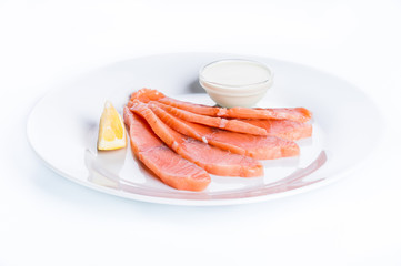 Thin slices of salmon fillet with lemon and sauce on a white bac