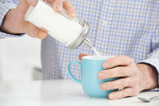 Mature Man Adding Sugar To Cup Of Coffee