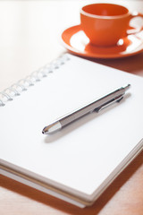 Pen on open blank white notebook with coffee cup on the desk