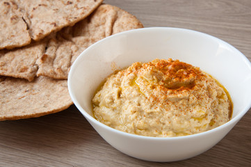 Home made fresh hummus in white bowl with pita flat bread. A delicious and healthy mediterranean side dish or snack.