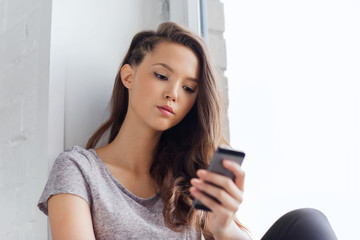 sad pretty teenage girl with smartphone texting