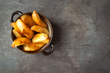 Bowl of chunky potato wedges fries served on a rustic stone, slate, gray table top.