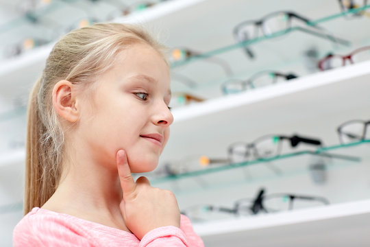 little girl choosing glasses at optics store