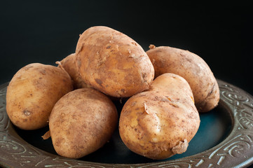 Plate of home grown potatoes piled on a rustic dish on a black table.