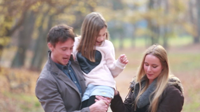 Family walking in park, father carries daughter in his arms and mom tickles her