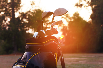 Golf clubs in golf bag on golf field at sunset