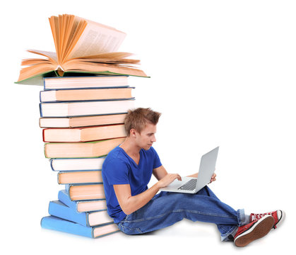Handsome young man with laptop sitting near stack of books isolated on white