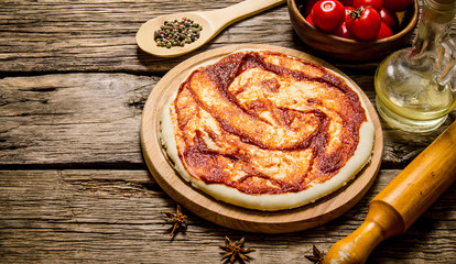 The rolled out pizza dough with tomato sauce, rolling pin and spices.