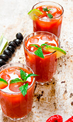 Cocktails made of tomatoes, vodka, ice, lime, pepper , salt and snack with celery and black olives on rustic background .