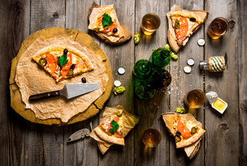 Pizza and beer for four people. On a wooden table.
