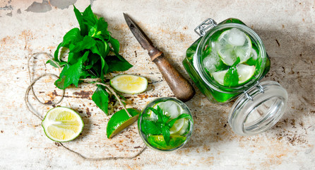 Ingredients for making mojitos - lime, mint leaves, rum, citrus knife and an old table.