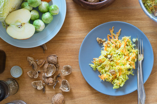 Savoy cabbage, brussels sprouts, apple, carrot and walnut salad on plate surrounded by ingredients