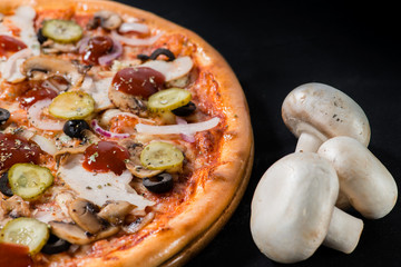 closeup Tasty pizza with mushrooms, ham and pickles on a black b