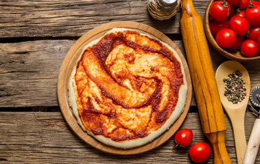 The rolled out pizza dough with tomato sauce, rolling pin and spices.