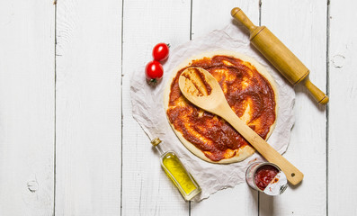 The rolled out pizza dough with tomato sauce and with a rolling pin.