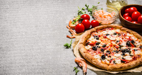 Seafood pizza with shrimp and tomatoes. On stone table.
