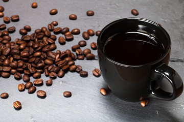 Black cup of coffee and coffee seeds on the slate background