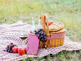 In a field a couple has placed a towel with a picnic basket. Around there are bottles of wine with...