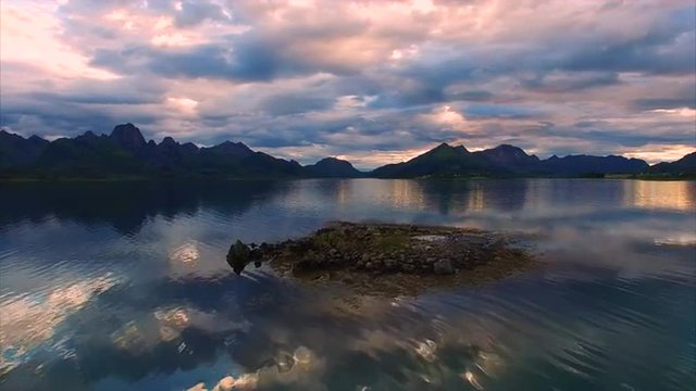 Flying low above rocky islet in fjord with the view of mountain peaks on Vesteralen islands on cloudy summer evening. Aerial 4k Ultra HD.