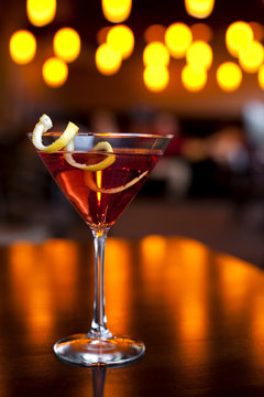 Cranberry Martini In Martini Glass With Lemon Peel Garnish And Twinkling Lights In The Background.