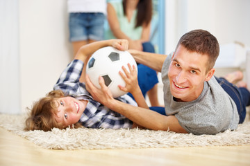 Vater und Junge toben mit Fußball im Wohnzimmer