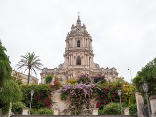 The baroque facade of the Modica's cathedral with several flowers in the foreground