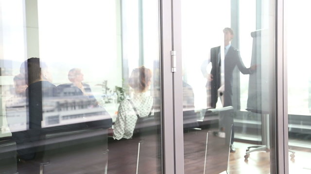 Businessman giving presentation using flipchart behind glass wall 