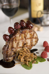 Grilled pork chop in balsamic raspberry sauce, with crispy onions, fresh greens and fruit, served with red wine.