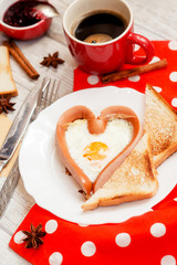 
romantic breakfast , heart-shaped fried eggs with sausage with toast, jam , hot black coffee , orange juice and spices on a wooden background