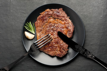 Ribeye steak with rosemary and garlic on black plate. Top view