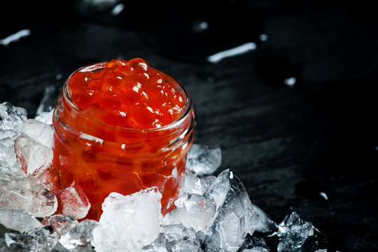 Delicious red caviar in a glass jar on crushed ice on black ston