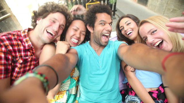 Five young adults laughing while taking a group selfie