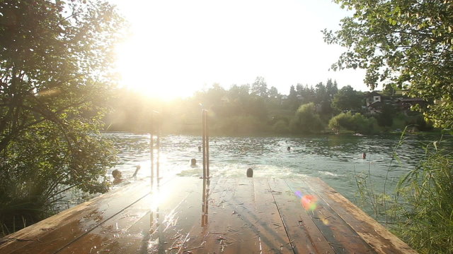 Back view of four young friends jumping into water from river dock at sunset
