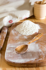 wooden spoon and a handful of flour on a cutting board and rolling pin with a mortar and pestle on the table. the concept of a rural bakery, selective focus