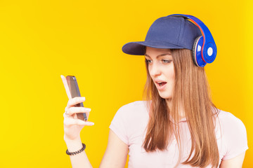 Surprised teenage girl uses a headphones and mobile phone